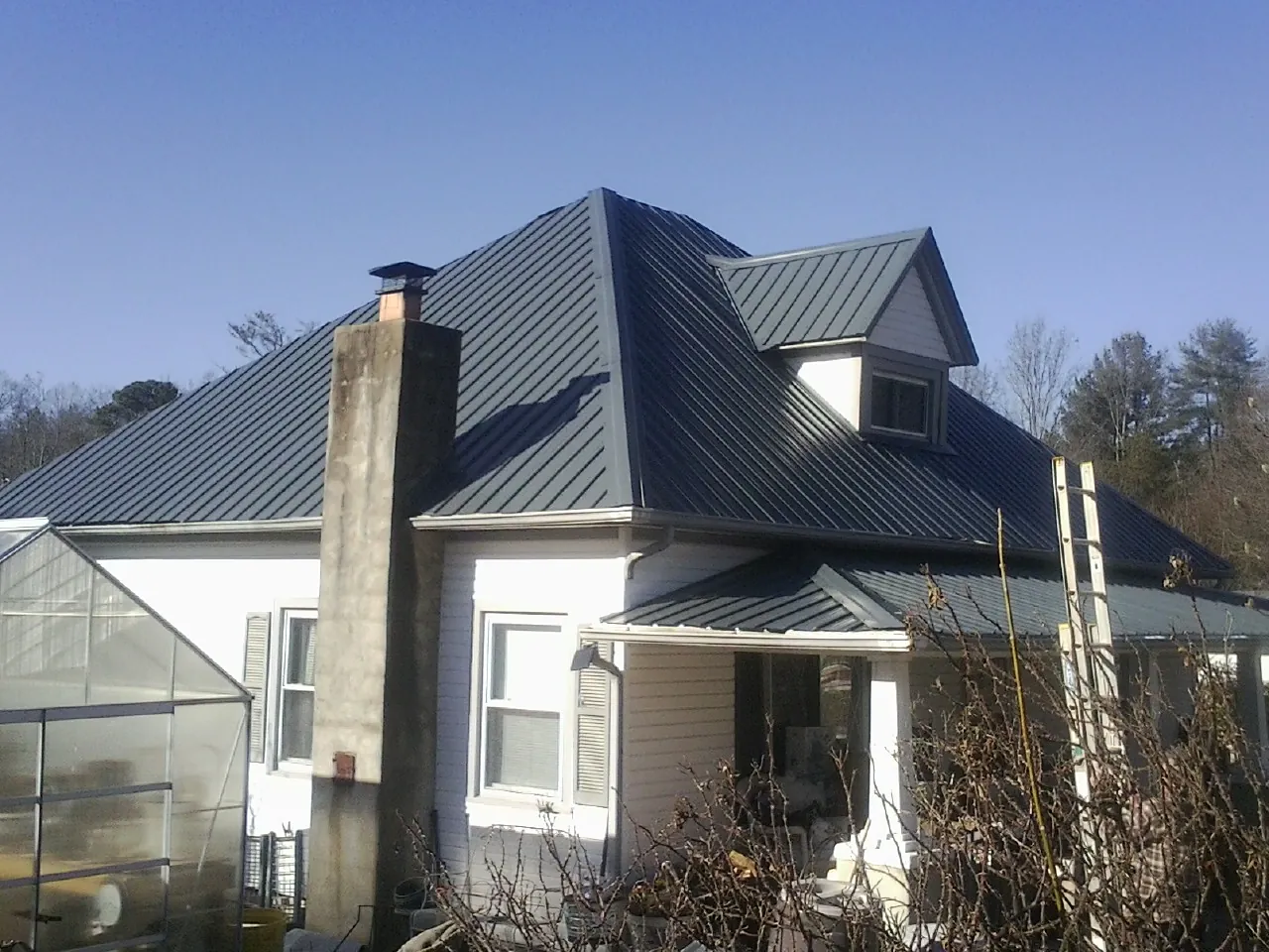 Dark blue standing seam metal roof on a white farmhouse with dormer — Slate & Tile Roof Repair by Roofing Brothers in Saint Anne