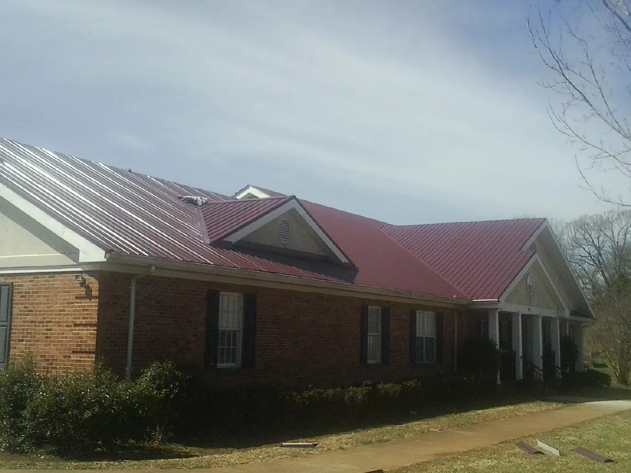 Red metal roof with gabled entries on a long brick building, from a Hail Damage Roof Repair job in Saint Anne