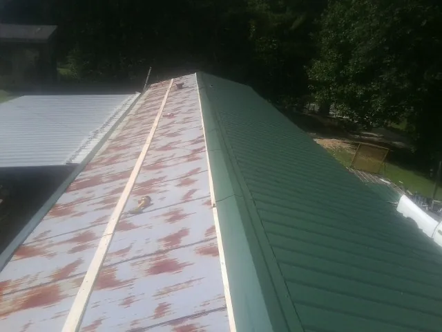 Old rusted panels beside newly installed green metal roofing — Wind Damage Roof Repair by Roofing Brothers in Saint Anne