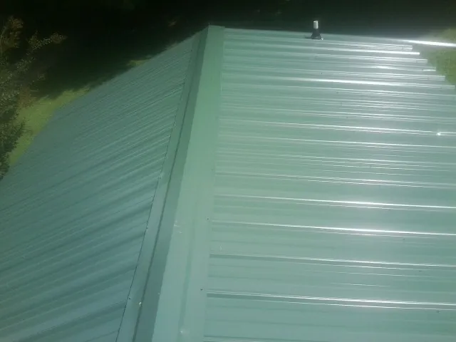 New green metal panels meeting at the ridge of a roof — Flat Roof Repair work by our crew in Saint Anne