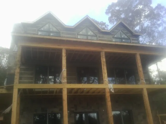 Dormers and porch framing on a large log home under construction — Roof Coating work by our crew in Saint Anne