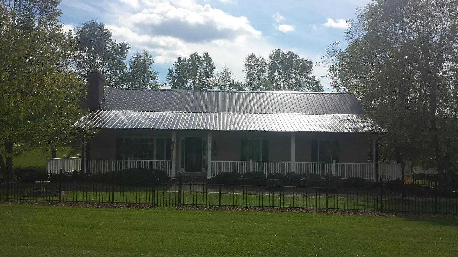Gray metal roof on a brick ranch with a full width front porch — Gutter Guard Installation work by our crew in Saint Anne