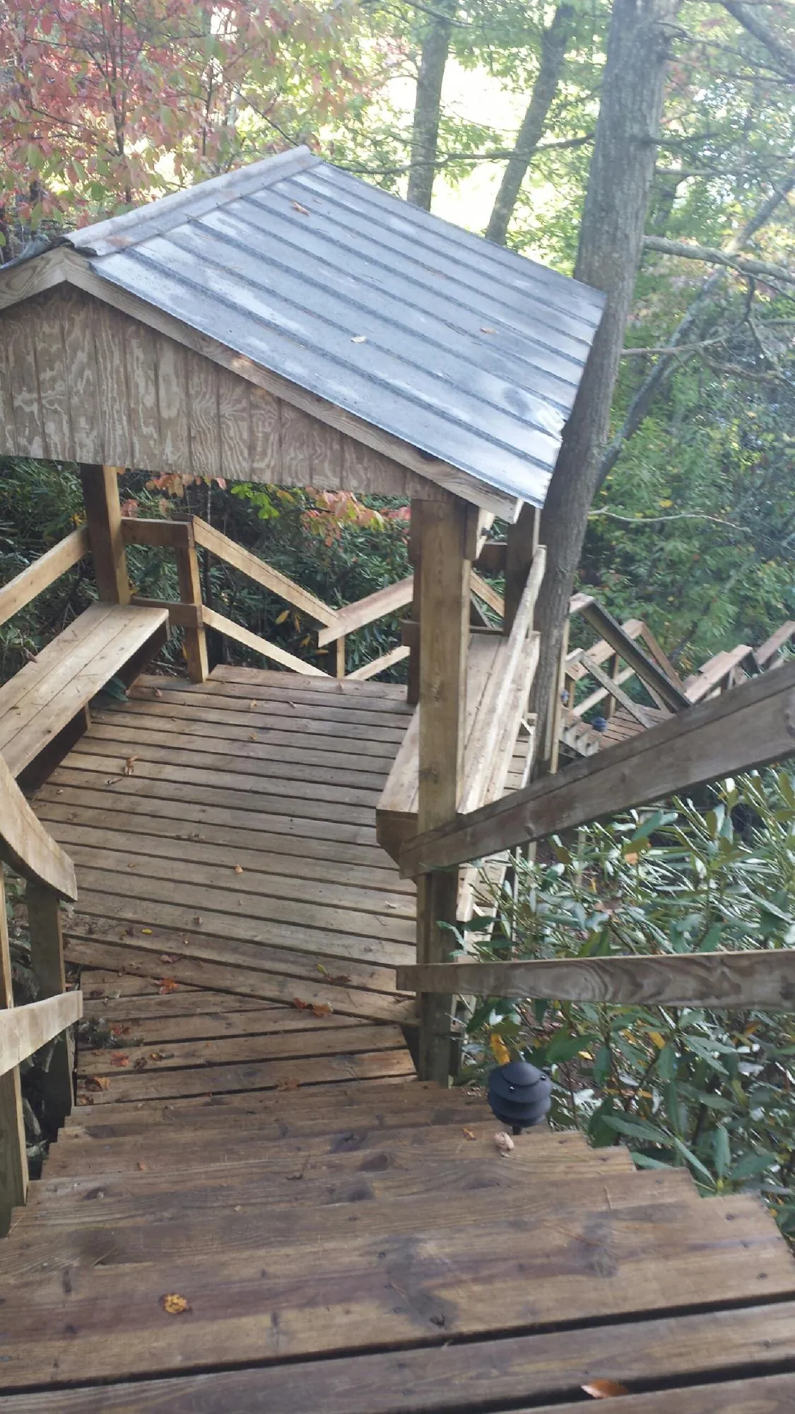 Metal roofed shelter over wooden steps on a wooded walkway — Skylight Repair & Installation work by our crew in Saint Anne