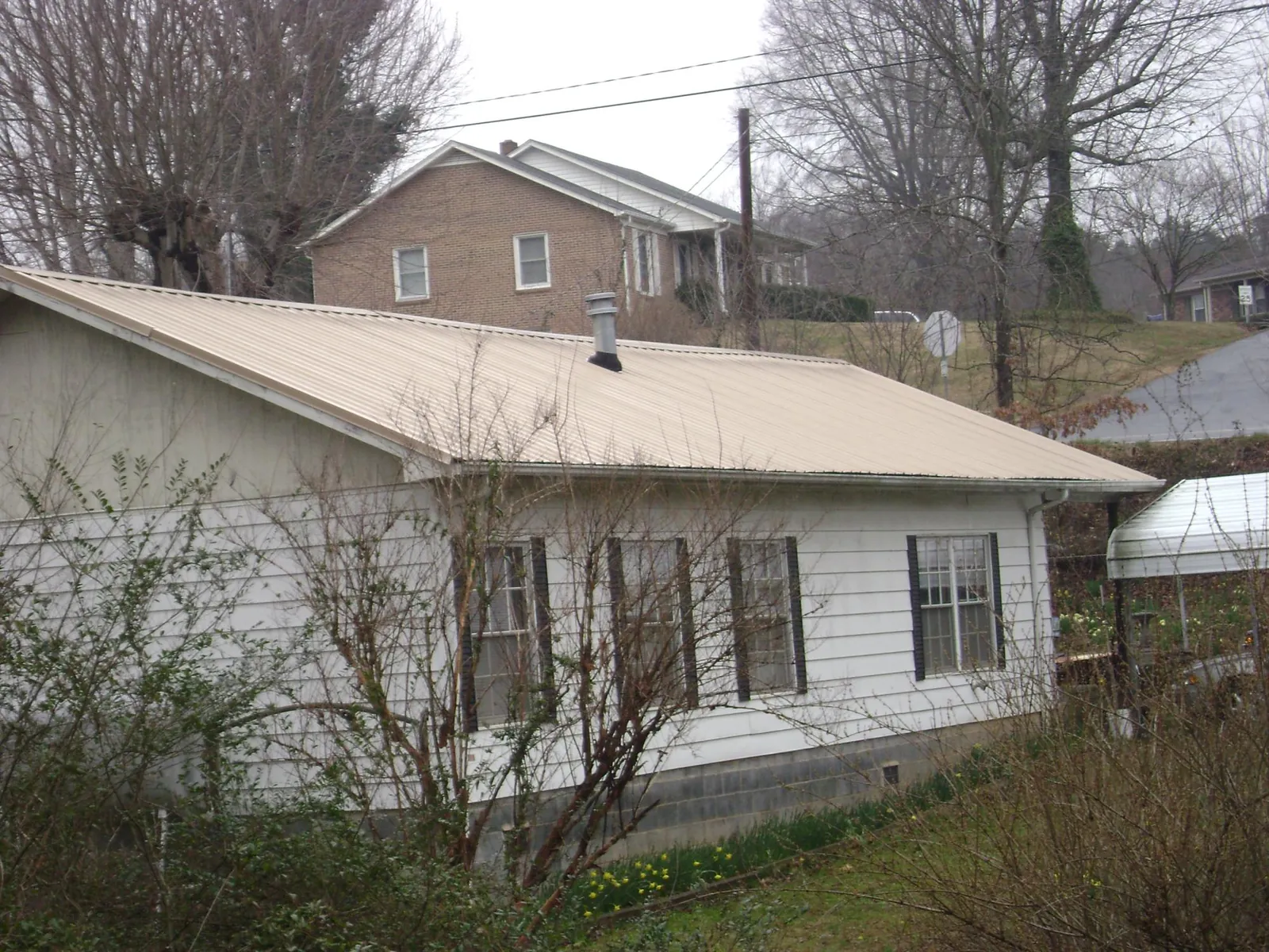 Tan metal roof on a white sided house set into a hillside — Commercial Roofing by Roofing Brothers in Saint Anne