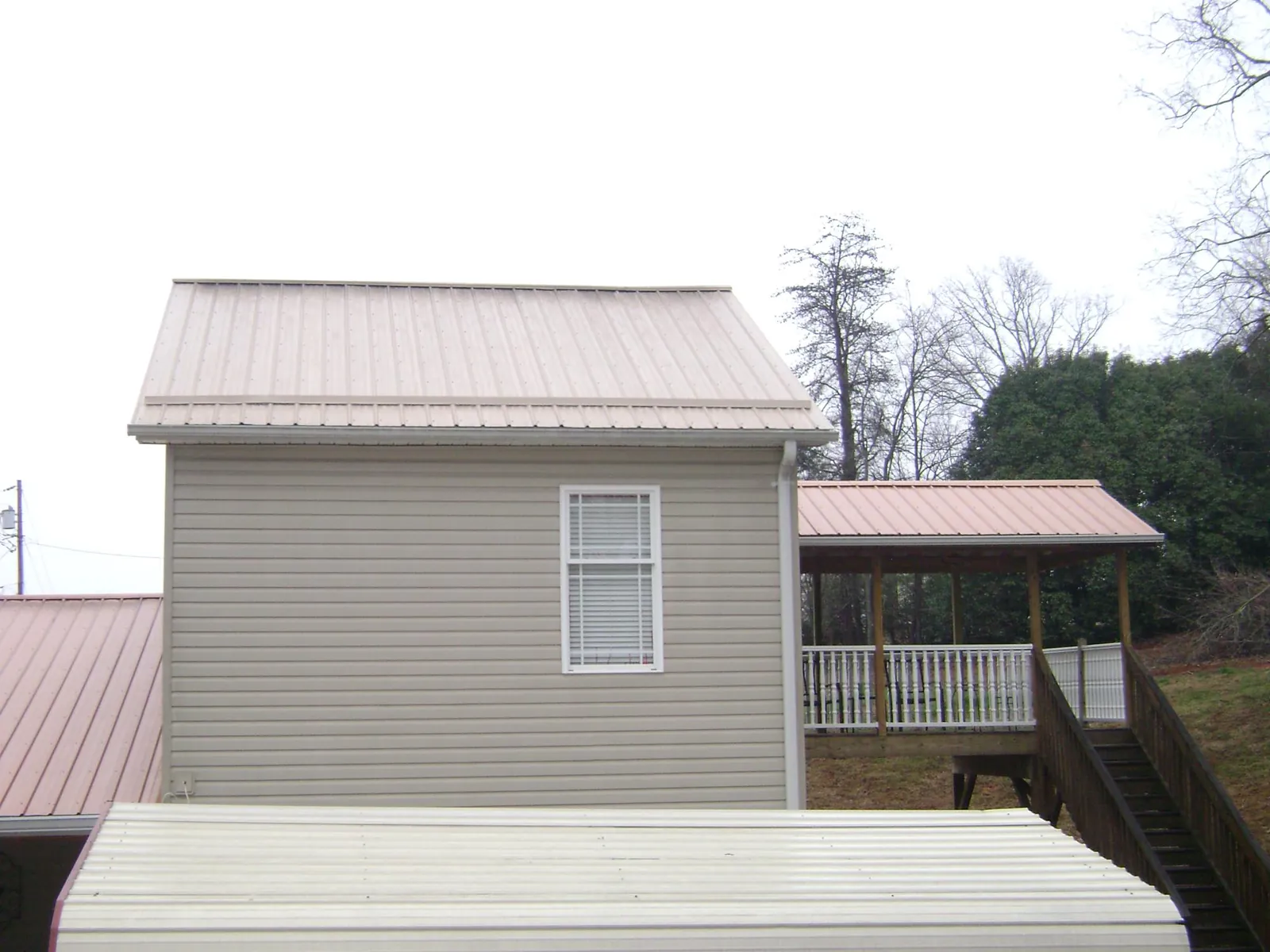 Tan metal roofs on a two story addition and attached porch, from a Roof Replacement job in Saint Anne